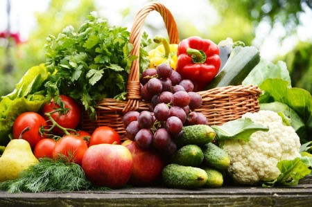 Variety of garden vegetables and fruits in and surrounding a basket on a table.
