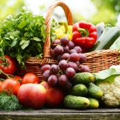 Variety of garden vegetables and fruits in and surrounding a basket on a table.