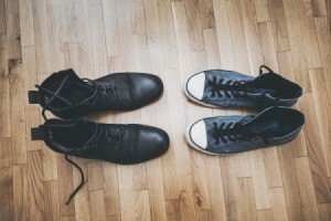 Pair of black boots and tennis shoes on a vinyl floor