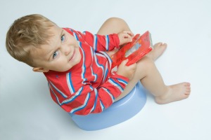 Toddler boy sitting on potty chair holding a book