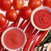White bowls of tomato paste, tomato sauce, and salsa setting on a background of tomatoes and red and green peppers