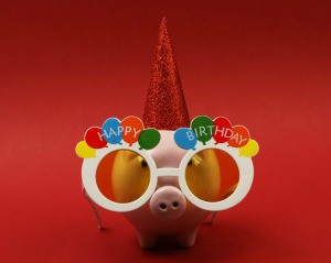 Piggy Bank wearing Happy Birthday glasses and a party hat against a red background