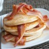 Pancakes layered with slices of bacon, topped with bacon on a white plate