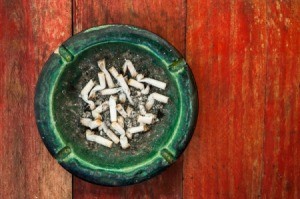 Ashtray full of cigarette butts on a painted red wooden table.