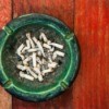 Ashtray full of cigarette butts on a painted red wooden table.