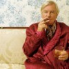 Man in dressing robe smoking cigar with wallpaper in the background
