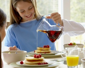 Girl pouring syrup on pancakes from a clear pitcher
