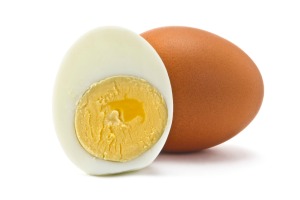 One brown egg and one half of a peeled hard boiled egg against a white background