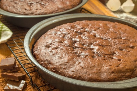 Two chocolate cake layers in pans on a cooling rack