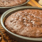 Two chocolate cake layers in pans on a cooling rack