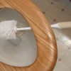 toilet brush suspended under toilet seat over bowl