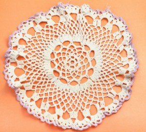 White doily with purple edges against an orange background.  Doily does not appear to be starched