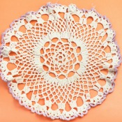 White doily with purple edges against an orange background.  Doily does not appear to be starched