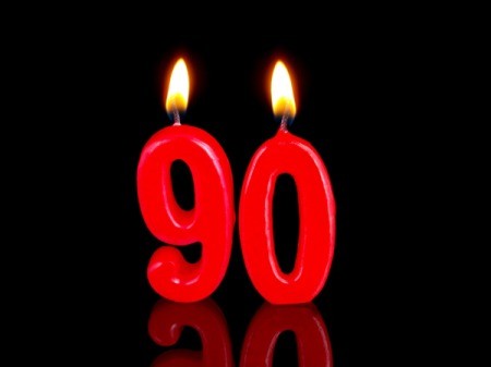 Lit candles in the shape of "90" against a white background