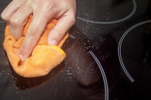 Hand holding orange sponge cleaning glass stove top
