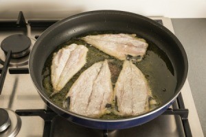 Fish fillets being fried in hot oil in a frying pan on stove