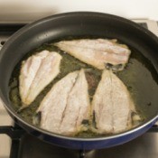 Fish fillets being fried in hot oil in a frying pan on stove