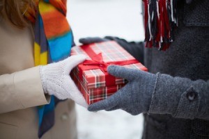 Hands of two people in winter coats and gloves exchanging a gift.