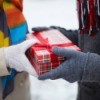 Hands of two people in winter coats and gloves exchanging a gift.