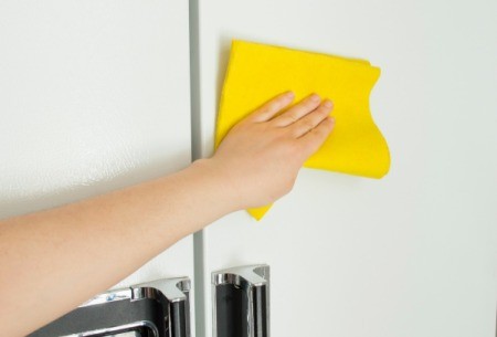 Hand cleaning the front of a refrigerator with a yellow cloth