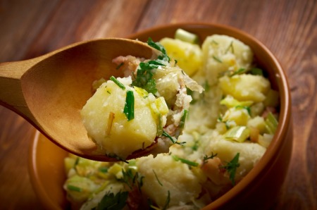 Spoon holding german potato salad over a bowl of same.