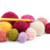 Several different color rolls of yarn with a crochet hook against a white background