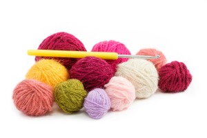 Several different color rolls of yarn with a crochet hook against a white background