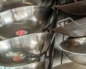 Close up of racks of woks for sale.  You can see the sticker reflected from the inside of the pan