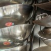 Close up of racks of woks for sale.  You can see the sticker reflected from the inside of the pan