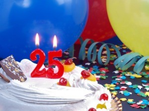 Candles in the shape of the number 25 on a cake in front of balloons, confetti and streamers