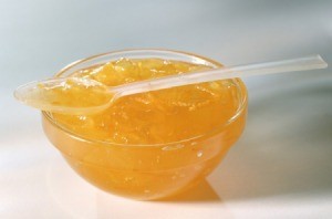 Orange Jelly (or marmalade) in a glass bowl with a clear plastic spoon of jelly laying across the top