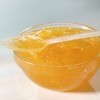 Orange Jelly (or marmalade) in a glass bowl with a clear plastic spoon of jelly laying across the top