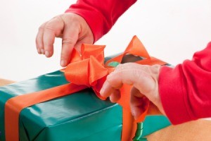 Hands opening a wrapped green gift with a red bow.