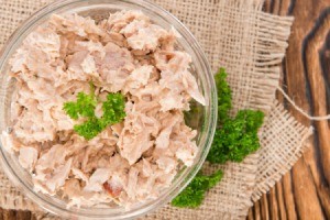 Clear glass bowl of dry looking tuna salad, garnished with parsley.