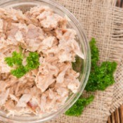 Clear glass bowl of dry looking tuna salad, garnished with parsley.