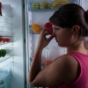 Woman holding nose while standing in front of open refrigerator door