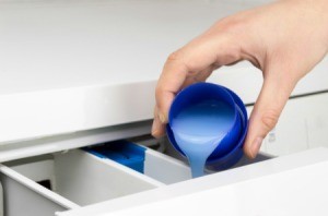 Hand pouring fabric softener into washing machine compartment