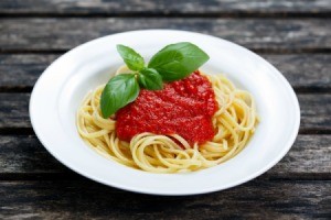White pasta bowl with spaghetti pasta, marinara sauce and a sprig of basil