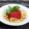 White pasta bowl with spaghetti pasta, marinara sauce and a sprig of basil