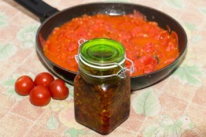 Pan of spaghetti sauce with jar of chili sauce and tomatoes in front