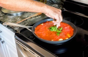 Hand placing basil leaves in pan of spaghettis sauce on stove