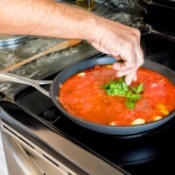 Hand placing basil leaves in pan of spaghettis sauce on stove