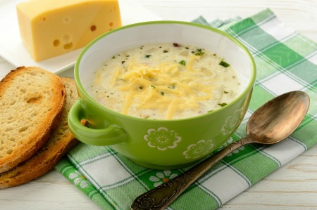 Bowl of cheesy potato soup with shredded cheese on top in green bowl on a green plaid napkin