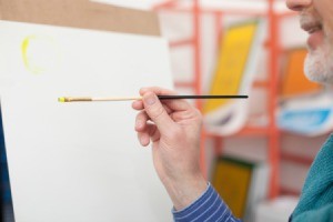 Man with grey beard painting on an easel