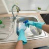 Hands in rubber kitchen gloves cleaning sink with several cleaning products