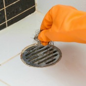 Orange gloved hands removing hair from a bath tub drain
