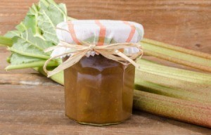 Jar of Rhubarb Marmalade with cloth covered lid in front of several stalks of rhubarb