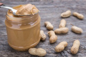 Jar of peanut butter with spoonful of peanut butter resting on top.  Peanuts are spread around the jar.