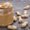 Jar of peanut butter with spoonful of peanut butter resting on top.  Peanuts are spread around the jar.