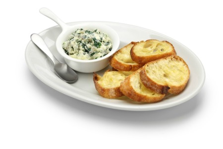 Dish of spinach artichoke dip and toasted baguette slices on a plate